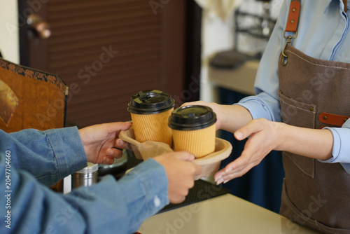 A barista hands a tray with two coffee cups to a customer in a warm cafe setting.