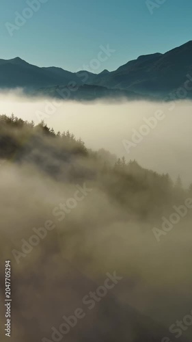 Aerial foggy mountain landscape with clear sky. Morning mist covering forest and hills. Vertical video 4k