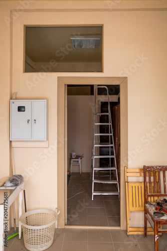 Room with a ladder, electrical box, and chairs, during renovation.
