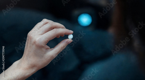 Close up of hand holding single medicine pill for anxiety depression or insomnia treatment on dark background