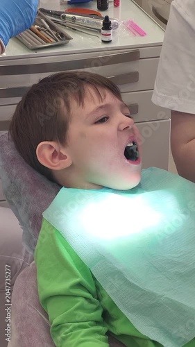 Dentist using suction tube to clean mouth of young boy patient sitting in dental chair. Pediatric professional medical checkup. Oral hygiene and healthcare procedure in dental clinic.