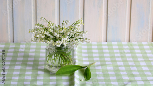 Foto Spring still life with lily of valley bouquet in glass jar on green checkered ta