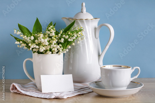 Bild auf Leinwand Business card mockup with blank white card beside lily of valley bouquet, porcelain coffeepot and cup on blue background, spring branding and space for your text