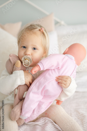 Vászonkép Baby with pacifier holding dolls