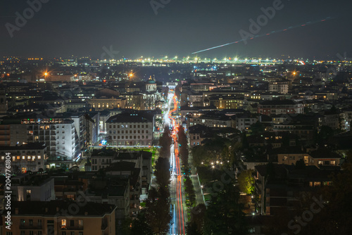 Nighttime view of Bergamo with illuminated tree lined avenue and domed landmark