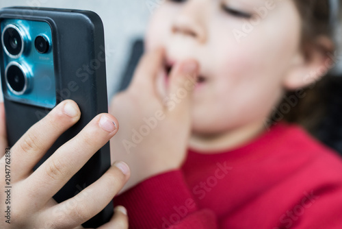 Bild auf Leinwand A young child holding a smartphone close to their face while touching their mouth, showing a concept of tooth pain, dental problem consultation, or using a mobile health app at home