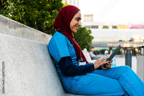 Arab woman wearing hijab and nurse uniform - Middle eastern doctor wearing hijab using tablet in hospital area