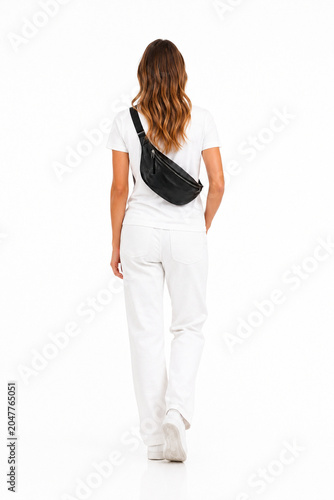Full-length rear view of a woman walking away, wearing an all-white casual outfit and carrying a black leather crossbody bag. Isolated on a clean white background, showcasing modern urban fashion, lif