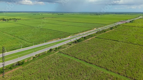 Aerial view of rural highway crossing vast green agricultural fields under cloudy sky