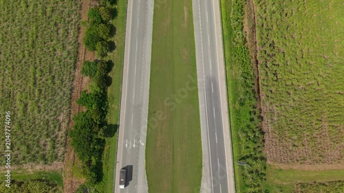 Aerial view of rural highway crossing vast green agricultural fields under cloudy sky