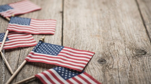 Small American flags arranged on a rustic wooden surface. The flags feature red, white, and blue colors, symbolizing patriotism and national pride.