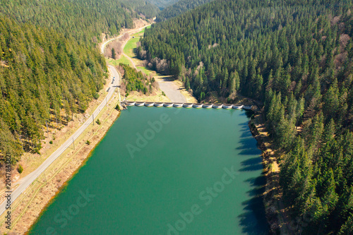 Drone view of a forest reservoir with turquoise water surrounded by dense evergreen woodland. Scenic landscape and water management infrastructure in the Black Forest region of Germany