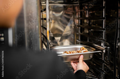 Cuadro en lienzo A chef slides a stainless steel tray filled with cooked food into a professional commercial combi oven in a restaurant kitchen