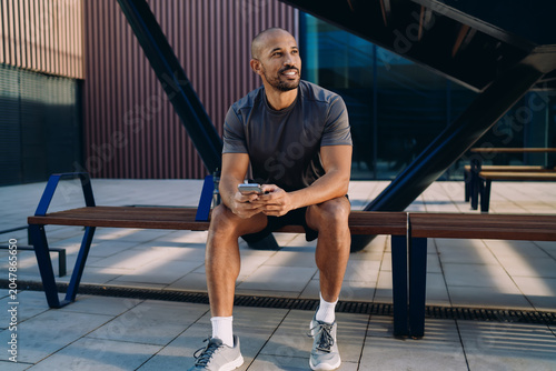 Smartphone held by athlete against blurred city background, person checking notification or fitness app after training, mobile connection and digital lifestyle, authentic representation, copy space.