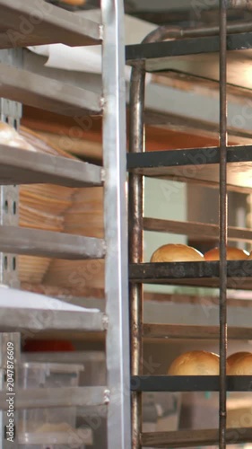 Vertical video: Shifting camera revealing metal multi-tier rack in bakery showing brown roll trays