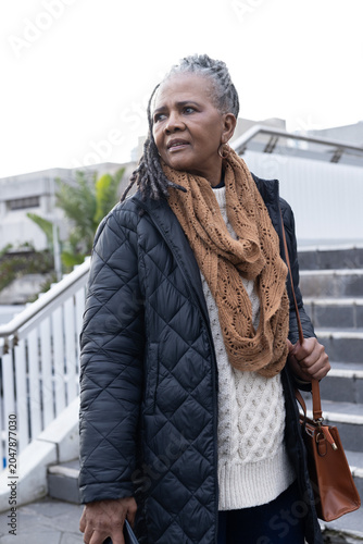 Vertical video: Senior African American woman pausing on steps looking left holding bag, blue item