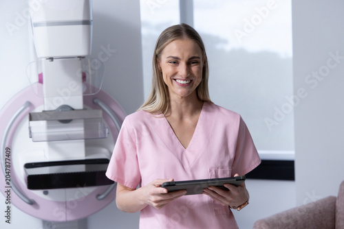 Cuadro en lienzo Adult woman in pink scrubs standing in imaging room beside mammography unit hold