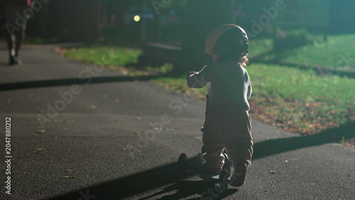 Bild auf Leinwand Toddler riding scooter at night in park, child wearing safety helmet on pathway