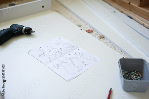 Foto Electric drill rests on a white surface next to assembly instructions, screws in