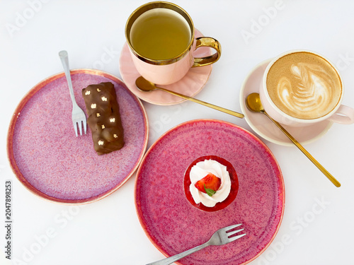 Top view of coffee latte art, green tea and gourmet desserts on pink plates over white background. High quality photo