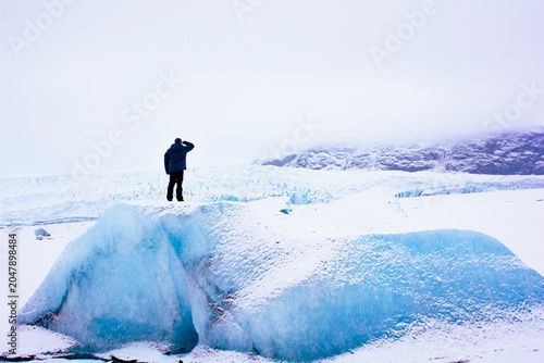 Explorer standing on giant blue iceberg looking at glacier in Iceland. High quality photo