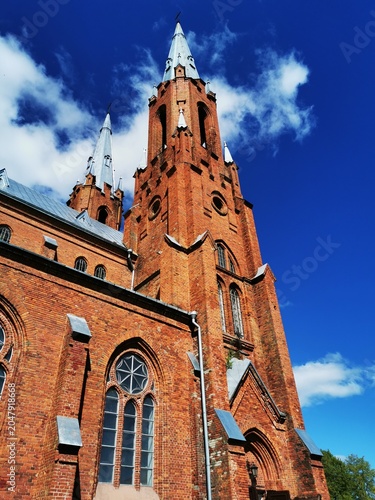 Fotografi Majestic neo-gothic red brick church tower against blue sky.