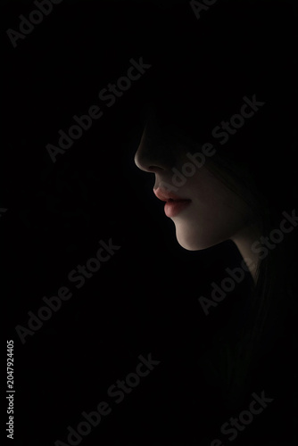 Minimalist close-up portrait showing a woman’s lips and chin in profile against a dark background. Soft lighting highlights the natural red tone of her lips, creating an elegant and mysterious composi