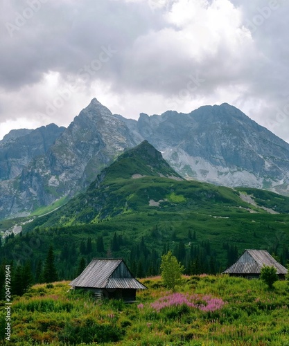 Foto Towering alpine peaks rise dramatically above rolling valleys and drifting clouds