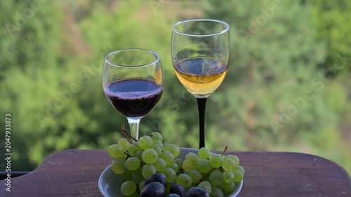 Fresh green grapes with wine glasses on a wooden table against a blurred lake view, static high-quality lifestyle footage