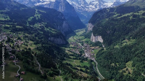 Drone panorama over Lauterbrunnen Valley, alpine village and green meadows beneath snowcapped Swiss Alps in summer.