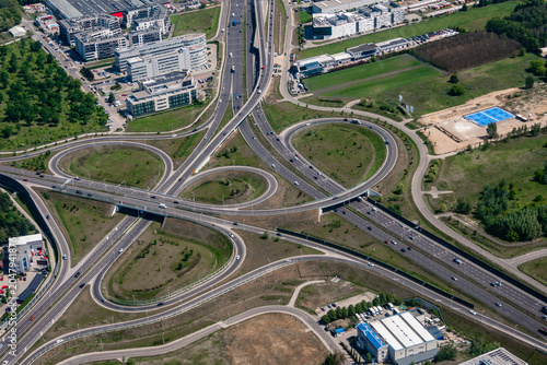 Obraz na plátně Aerial view of a cloverleaf interchange near Warsaw, Poland, with looping ramps, overpasses, office parks, warehouses, green space, and a bright blue sports court
