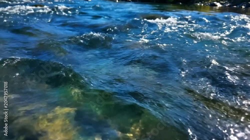 Close up view of crystal clear river water gently flowing with sunlight reflections and underwater rocks