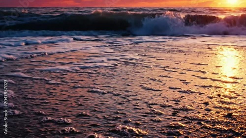 Ocean waves washing onto a sandy beach at sunset with vibrant colors and foamy water