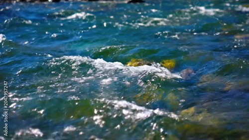 Close-up of a vibrant blue mountain river flowing rapidly over rocks on a sunny day