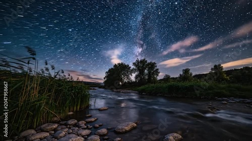Time-lapse of starry night sky with milky way galaxy over flowing river at dusk