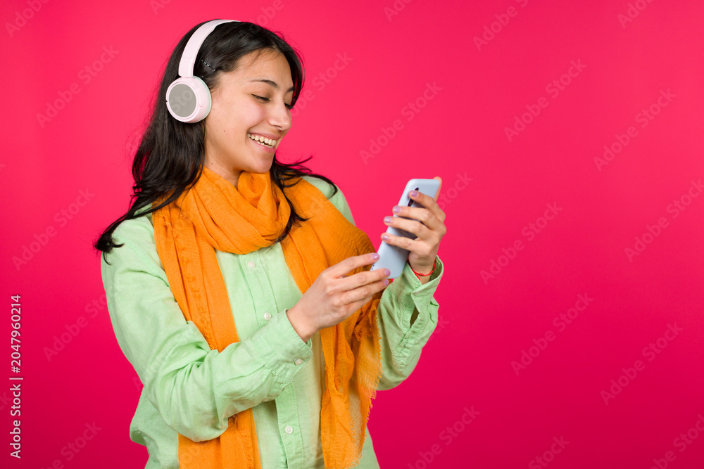 Naklejka premium Young woman smiling enjoying music looking smartphone