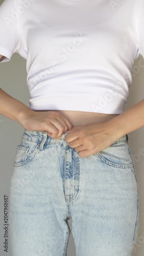 Woman trying to button tight jeans. Close-up of female body struggling with small jeans size at home. Video for wellness clinics, nutrition programs, weight management services and healthy lifestyle