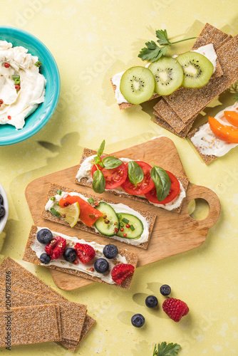 Fresh crunchy rye crispbreads with different toppings on green table, top view
