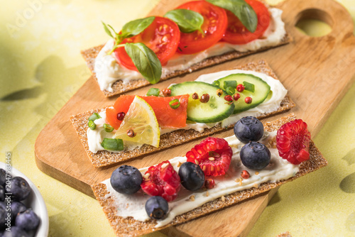 Fresh crunchy rye crispbreads with different toppings on green table, top view