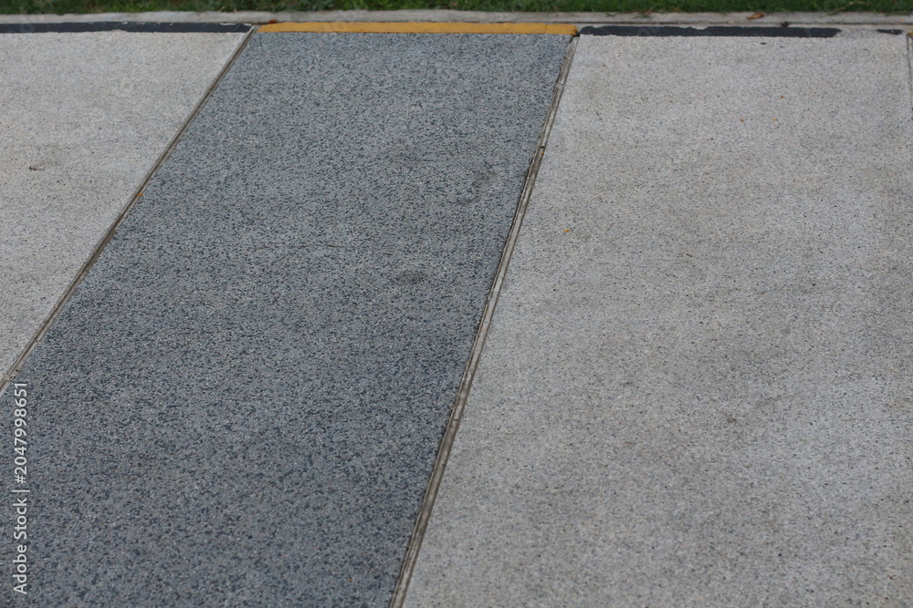 Fototapeta premium Textured concrete pathway with contrasting grey and light grey sections and yellow border
