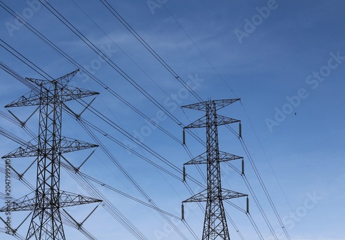 Towering electricity pylons against a clear blue sky with power lines stretching across