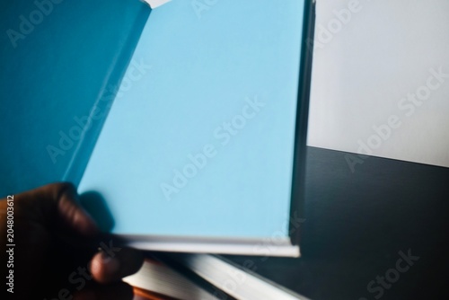 Fotografía A first-person point of view shot of a hand holding open a black hardcover book to reveal a blank, solid light-blue interior page over a dark background