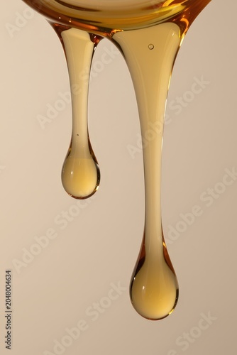 Golden viscous liquid dripping in slow motion, abstract, close-up. Use: food styling, cosmetic advertising, dessert photography.
