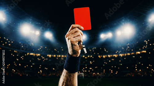 Referee's stern decision a red card raised high against the dramatic stadium lights, symbolizing an expulsion from the intense sports competition
