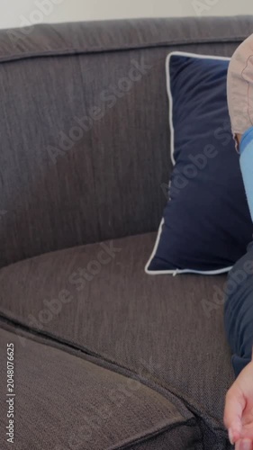 Vertical video: Pressing control, adult in beige shirt measuring BP on couch with cuff, copy space
