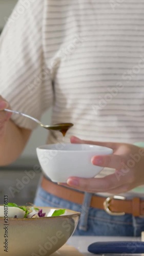 Vertical video: Mixing dressing in bowl, striped cook drizzling spoon for salad on kitchen counter