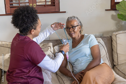 Obraz na płótnie Senior African American woman getting nebulizer on sofa as aide in scrubs holdin