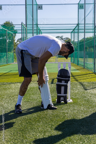 Cricket batting pads are resting beside portable stumps in sunlit netted practice bays A3 A4