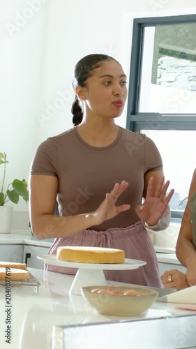 Vertical video: After clasping, baker in brown top showing spacing on cake at kitchen island