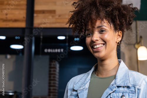 Foto African American woman in twenties smiling, glancing at cafe pickup with 'COLLEC